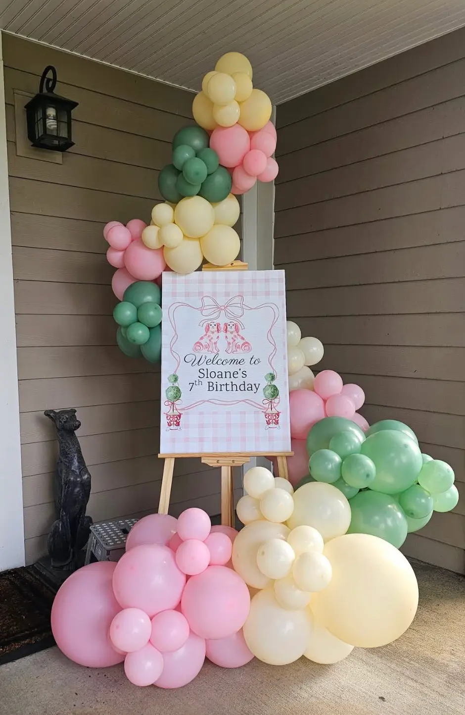 Pink, yellow and green balloons around a birthday welcome sign